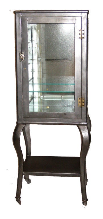 Glass cabinet on sexy curvy legs with wheels. Mirror on the back side and on the internal base layer. Can host two shelves. Stripped to the metal patina and coated to prevent rusting.