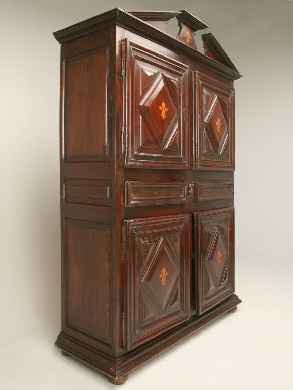 17th century (circa 1680) original antique French solid walnut, oak and fruitwood cupboard with hand laid fleur de lys decoration. This incredible cupboard offers gem cut doors, a broke pediment and original locks. Four cavern-like compartments are
