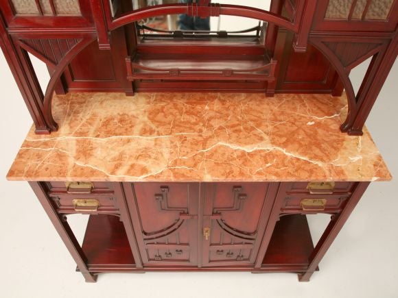 Aesthetic Movement red mahogany hutch from a suite comprising a dining table, chairs, and sideboard. The shaped and slightly flared cornice rests above textured glass paneled doors with carved geometric and naturalistic floral designs. A lower