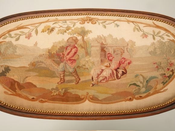 A Louis XVI fruitwood canape upholstered with the original Aubusson tapestry. This restored piece features an oval backrest with channeled framing. The upholstery, having a pastoral scene with figures, is in excellent condition. We restored the