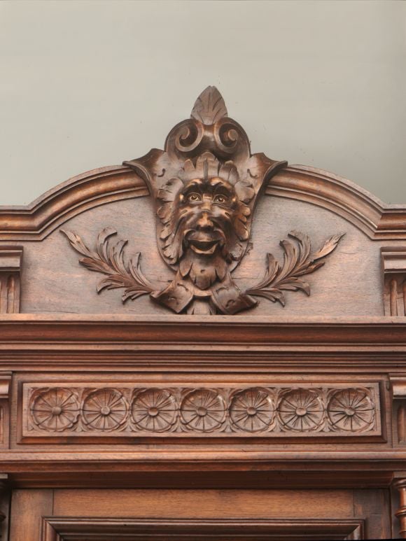 Henri II walnut hutch with crested pediment featuring center grotesque mask and turned gallery finished with urn finials at the side, above carved frieze with fluting and floral panels. The three fitted cabinet doors, with the original beveled glass