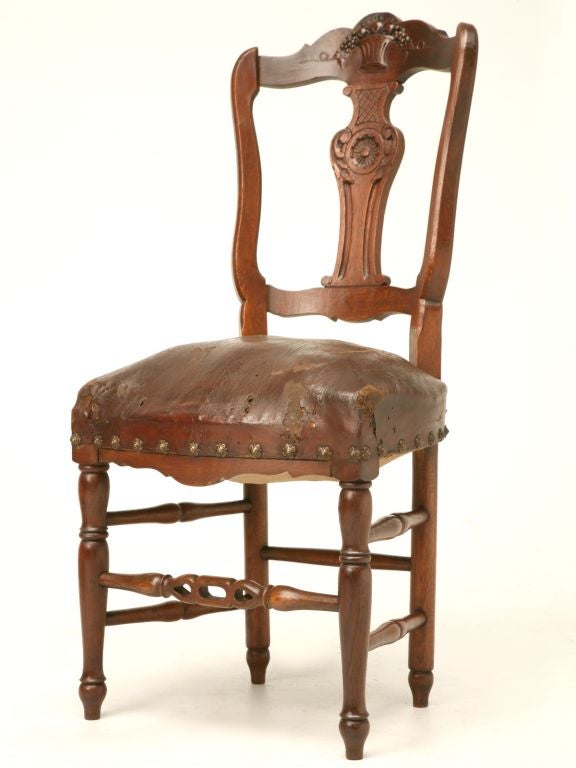 Beautiful antique French Louis XV style carved oak chairs with leather seats, pierced stretchers, a basket and fruit motif on the top of the backs followed by a centered sunflower flanked by acanthus leaves. Though in nice original condition, the