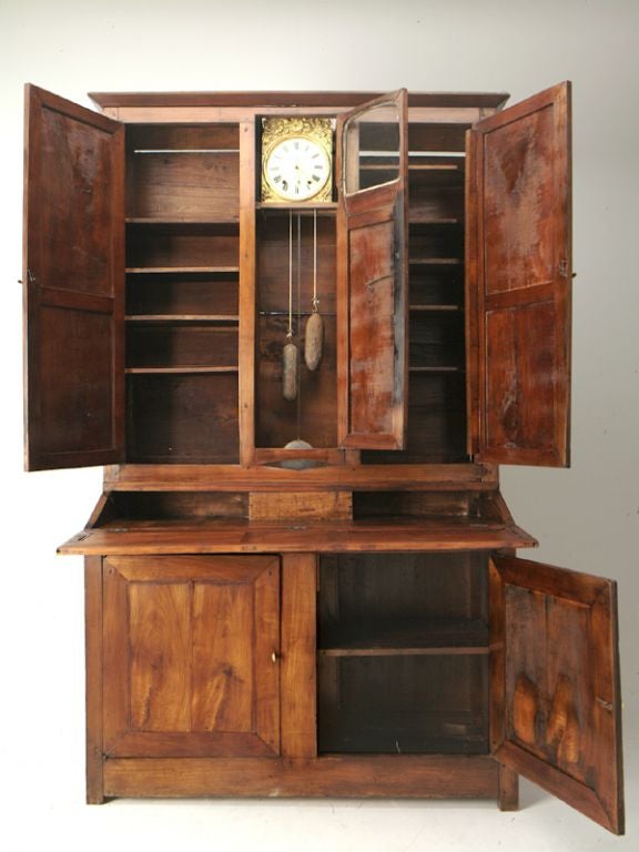 A provincial French cherry secretary abattante with a molded and flared cornice above the original Emile Chevassu clockface set into a brass repouse support. Two upper stage doors feature panel-in-frame construction and open to reveal ample shelving
