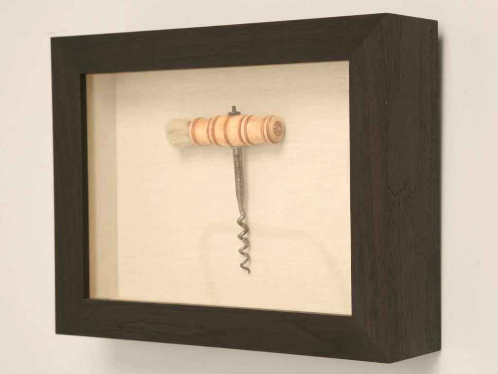 French corkscrew with a bone handle, a suspension loop and a dusting brush at one end. Mounted on linen in a coffee bean colored wooden shadow box. Great wine room accessory!