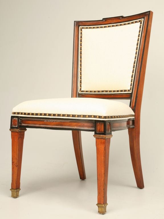 Directoire style chairs with white linen fabric, bronze nails over ribbon trim, black accents and an 'X' frame back with beveled edges that intersects at a bronze medallion. Also available with a white painted frame. Different fabrics are available.
