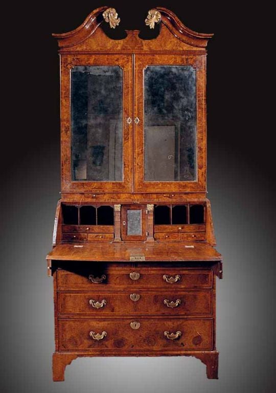 # F300 - George I burl walnut slope front bureau bookcase. This well preserved example has pleasing proportions and a lovely patination. The pediment  is hung with gilt leaf carved motifs. Below the frieze are two mirrored doors that are feather
