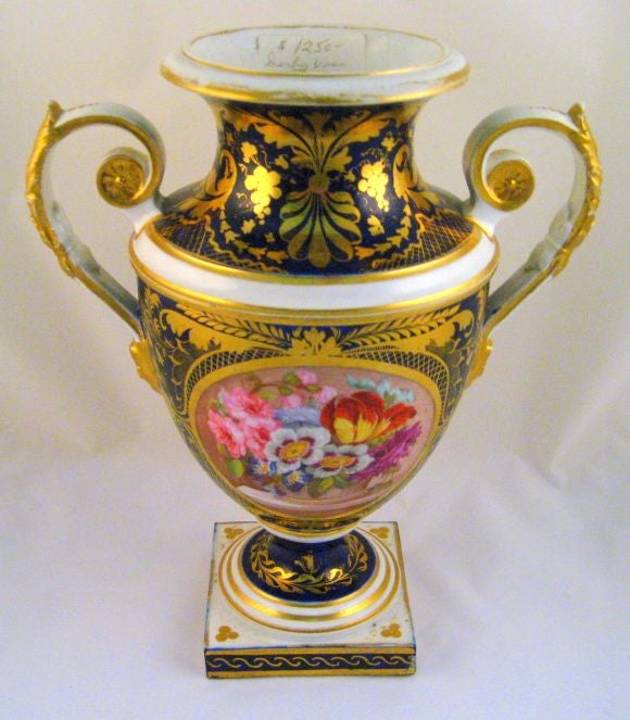 An exceptional Derby vase, with botanicals expertly painted on a central panel, and exquisite gilding applied on the front, base, and handles of the vase. <br />
<br />
The floral grouping is in the 'crushed hat' design of Moses Webster, which