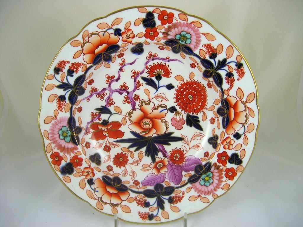 A finely-preserved pair of soup bowls by the Coalport (also: Coalbrookdale) factory, painted vividly in the Imari-influenced Regency fashion. The pattern features stylized foliage patterns and flowers, depicted in a surreal color scheme. The plate