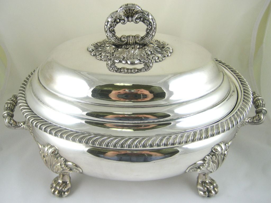 A finely formed Sheffield (silver-plate) vegetable tureen and cover, raised on paw feet. The central handle is formed with two facing scrolls, embellished with blooms and foliate designs. The four paw feet are formed as paws at their ends, and flow
