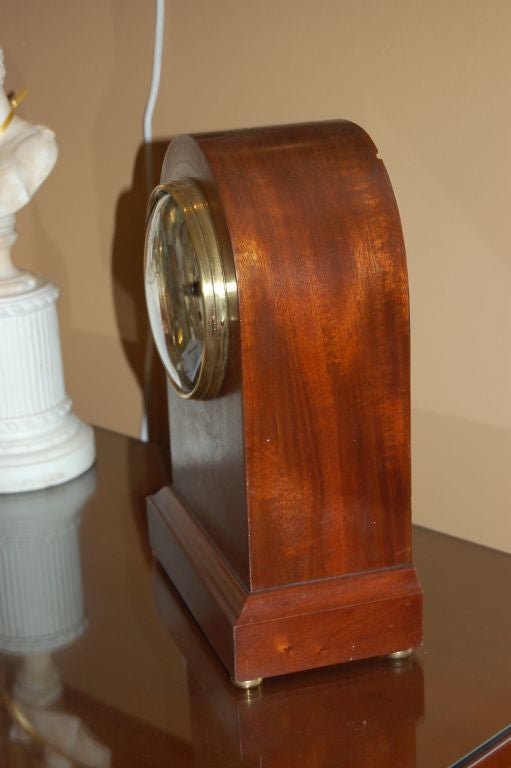 Classic clock-face design with plate-cover of glass and brass; mahogany with inlaid design of fruit and flowers; brass feet.