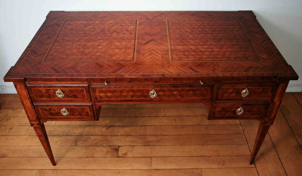 The whole having Rosewood and exotic wood parquetry, the top above a hidden leather writing slide with one central drawer flanked by two stacked drawers all with brass escutcheons all on tapered legs.