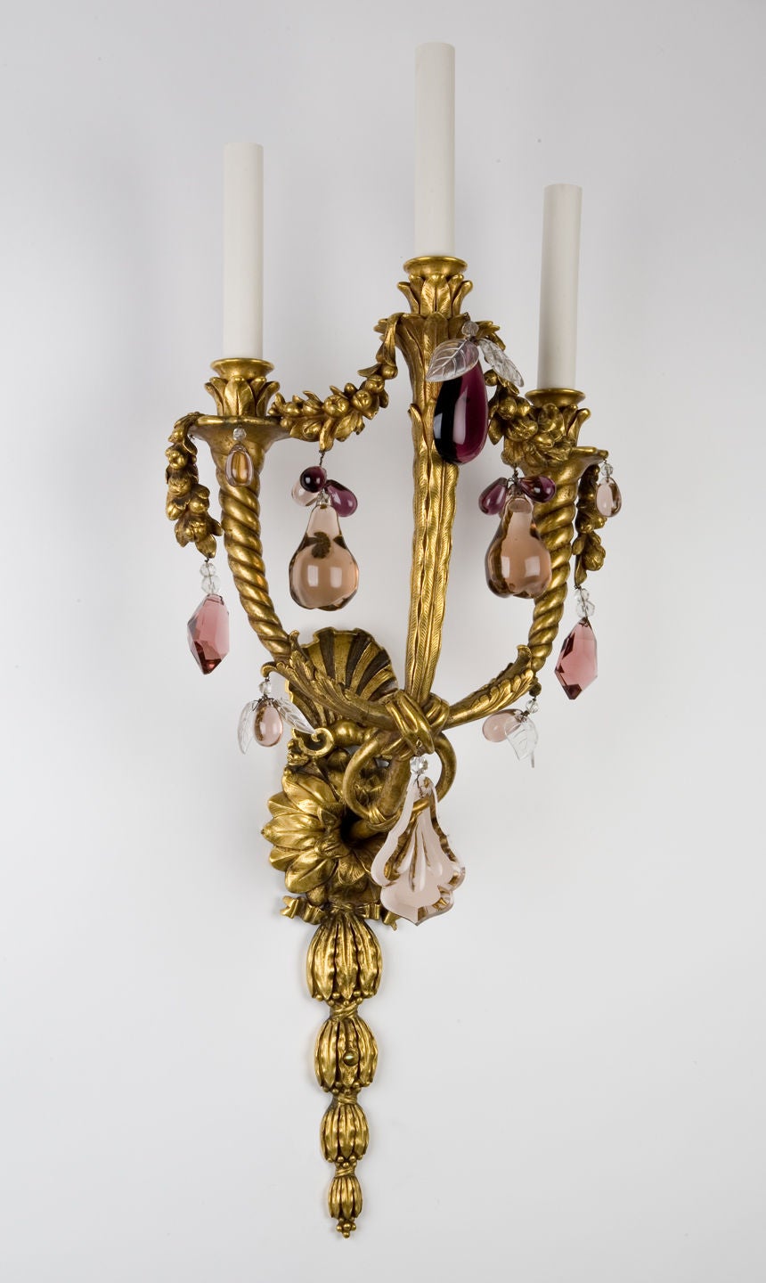 AIS2374

A pair of three light wall sconces in their original wonderful aged gold finish. Detailed with foliate, ribbon, and shell castings as well as fruited swags between the twisted, flared arms. Dressed with amethyst and clear crystals. From