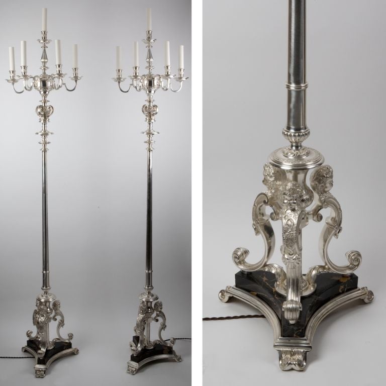A pair of 5-light floor candelabra lamps in silvered bronze. The tripod cupid bases stand on black marble plinths. The gadrooned and tapered standards support finely chased rectangular arms and arabesque-detailed waxpan and candle-cups.<br />
<br