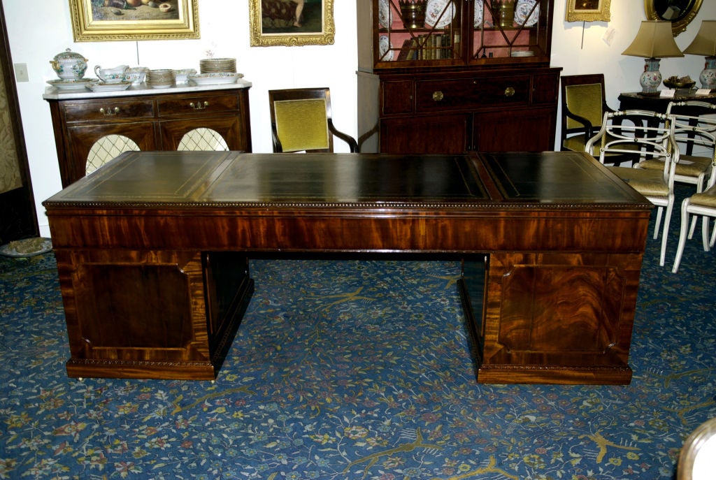 The shaped top with a leather tooled surface over three drawers resting on two pedestals with cupboard doors opening to a fitted interior.