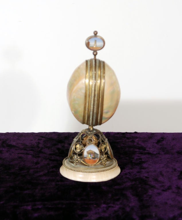 The bronze mounted Mother of Pearl shell, opening to a set of four petite perfume bottles. (two bottle tops missing)Decorated throughout with views of Paris, all on a marble base.