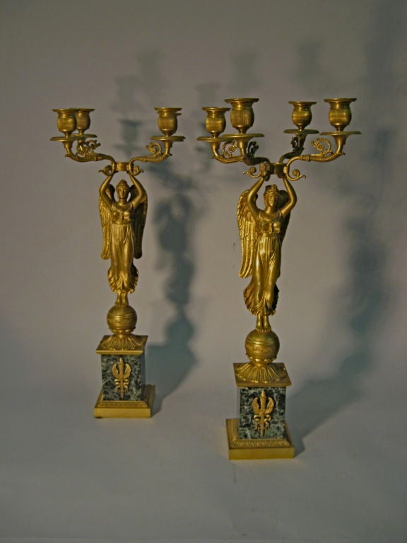 A very fine pair of gilt-bronze candelabra, the four candle-holders supported by allegorical figures of Winged Victory. <br />
<br />
Dating from the Empire period, each crisp formed bronze statue is mounted on a striated green marble base. The