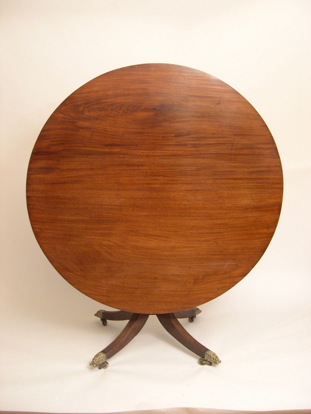 A fine Regency period tilt top pedestal round table in mahogany with reeded edges and legs, retaining its original brass recumbent lion-form caps and castors.