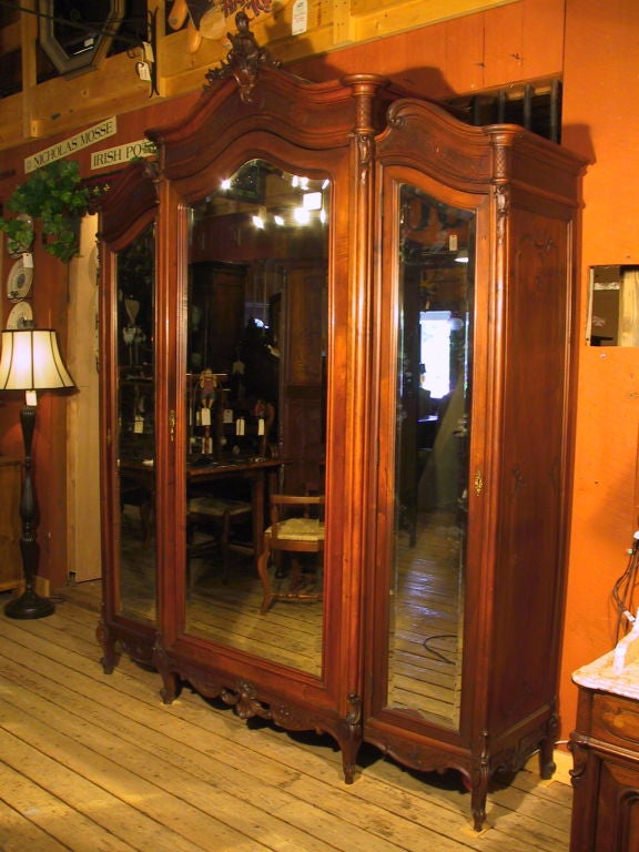 Antique Italian walnut triple door armoire with 3 large beveled mirror doors, ornately carved bonnet tops and side panels- intricately hand carved crest & base - original finish beautifully maintained - presents rich walnut color & patina.