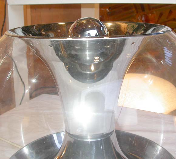 A lamp with a glass sphere and central hourglass chrome metal shade, chrome metal base with one bottom interior light and one top light. Wire with two position switch.