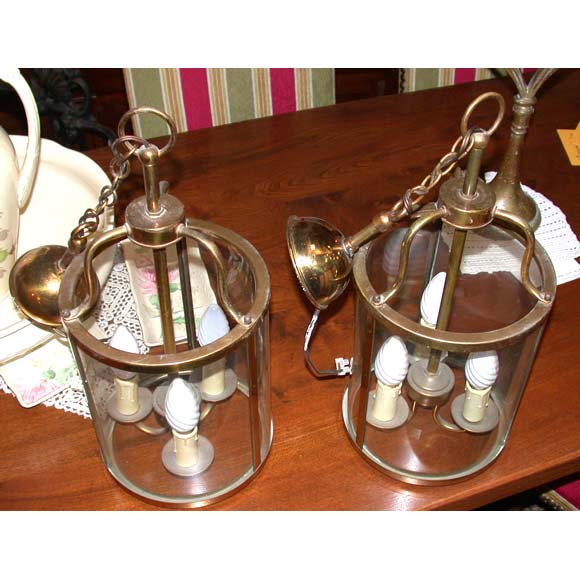 A pair of brass framed lanterns each with three curved glass paned sides and three central candle lights. The height of the lantern without the hanging chain is 48cm (18,90