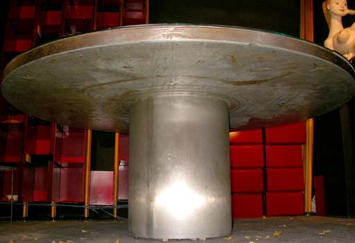 A large dining table on a central round base in metal, metal plateau with four quarter mirrored thick glass outer sections and chrome metal framed center rotating plateau 