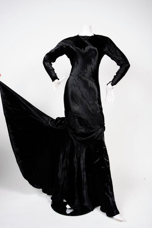 Circa 1930's Black satin bias cut gown with long sleeves and point at the wrists. Black satin buttons with loop closures. Same buttons down the back to end of back. 3 crepe bows on sides just above knees and at backside gathering the satin to create
