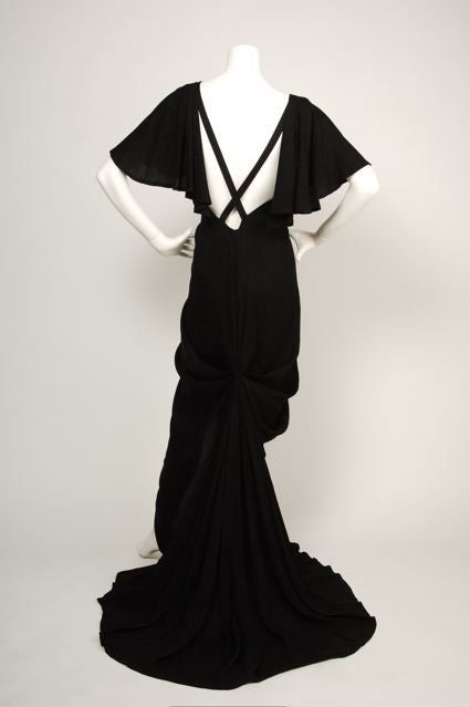 Black floral silk jacquard couture gown with a deep v-neck and bustle back full train. 1930’s inspired rock star glam. Pearl drop detail at v-neck.<br />
<br />
ABOUT EMANUEL UNGARO<br />
<br />
Born to Italian parents who had fled to France