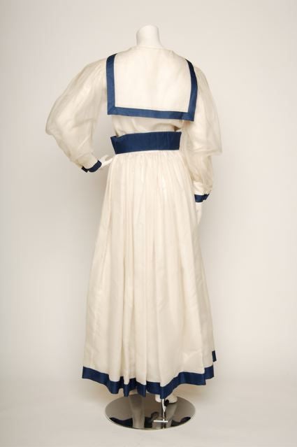 NORMAN NORELL<br />
<br />
Late 1960s/early1970's- 100% silk organza? White dress with blue trim sailor collar and large red bow neck tie. Full sheer organza puff sleeve, tight wrist with blue trim. Full skirt with blue trim at hem. Has matching
