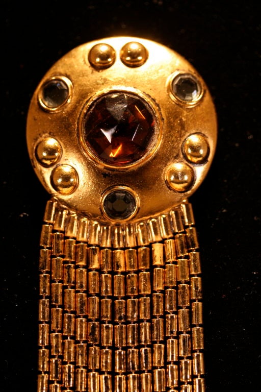 Dramatic gold tone metal fringed pin with dark amber faceted glass center stone accented by three faceted blue-gray glass gems. Attached to this round 1 7/8