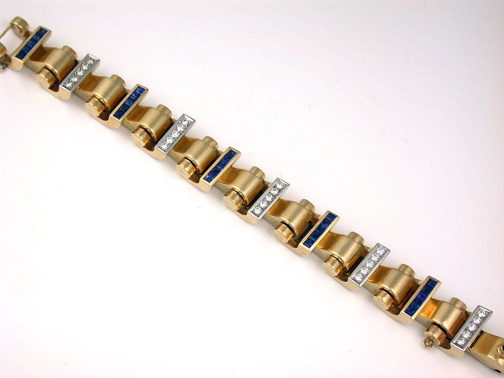 A 14 karat yellow gold, sapphire and diamond bracelet.  Signed Tiffany & Co.  The bracelet is done in a scroll like design set with alternating sections of sapphires and diamonds. The bracelet is set with a total of 25 diamonds weighing