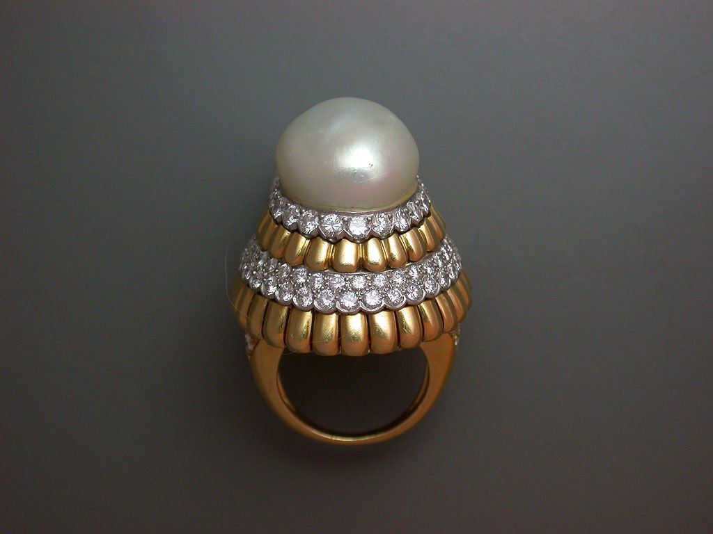 The conical, high-dome cocktail ring set at the top with a large, white baroque pearl (16mm), above concentric rings of polished yellow gold ribs and pave-set diamond rings set in white gold, with diamond shoulders. Signed VC&A, #41281, circa 1970.