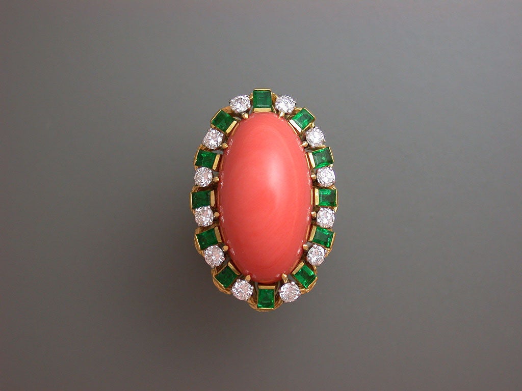 The colorful cocktail ring set to the center with a long oval orange coral cabochon, within a border of circular-cut white diamonds and square-cut gem emeralds all set in an attractive textured yellow gold mount, signed VCA for Van Cleef & Arpels,