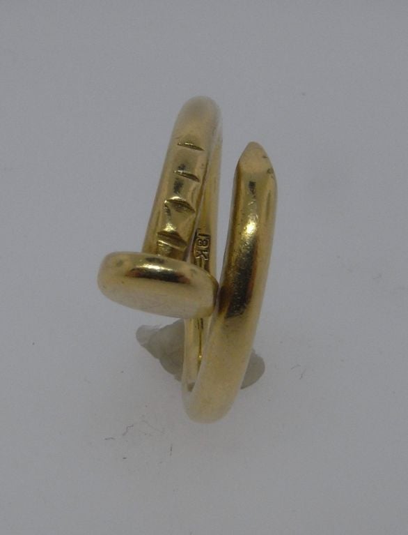 A gold ring designed as a bent nail to encircle the finger.  The band of the ring is 3mm in diameter, ending in a nail head of 7mm diameter.  The design is by Aldo Cipullo, who worked for Cartier in the 1970's.  Marked 'Cartier', '18k' and '1972',