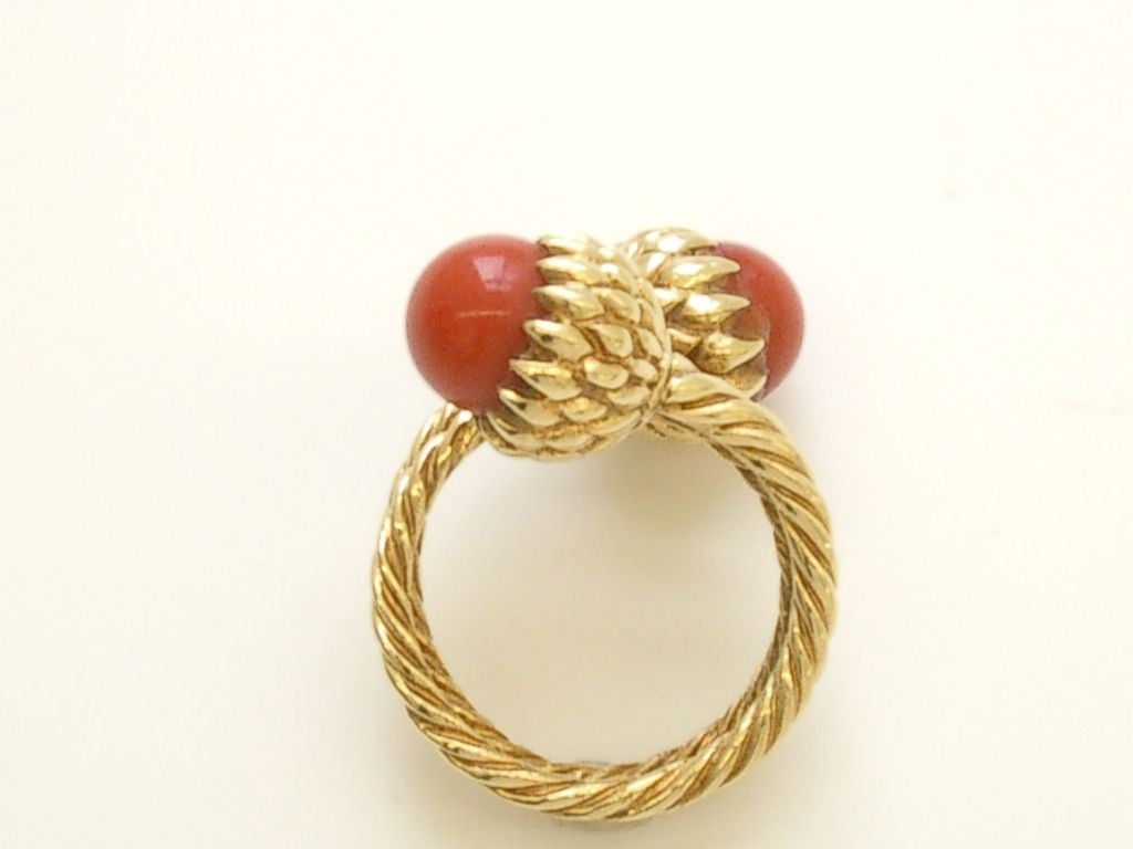 A stylish crossover 18k yellow gold and blood coral ring by Jean Schlumberger for Tiffany and Company. The twisted band ring culminating in two stylized pods each holding a brilliant burnt orange coral ball. <br />
Easy to wear. size 8.5
