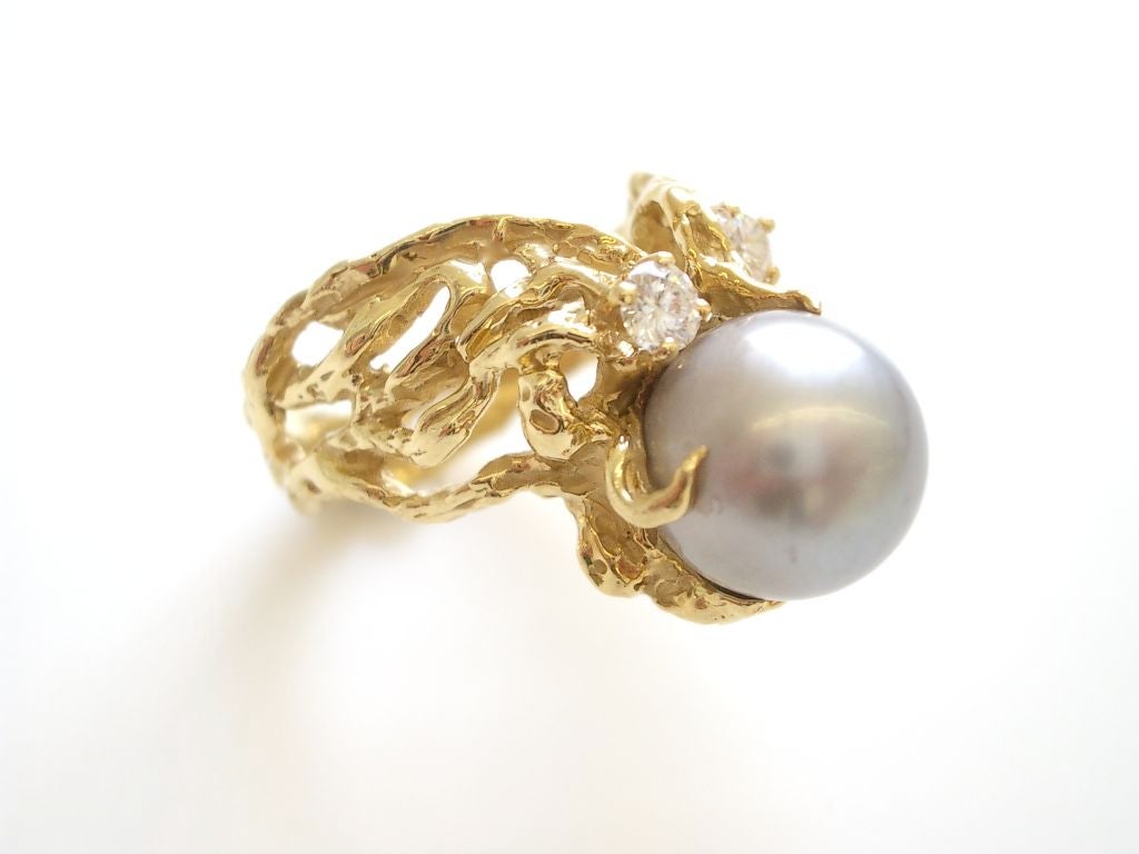 A pretty 18k yellow gold diamond and Tahitian pearl ring by Arthur King. The round 10.4mm light gray pearl with no blemishes and light pink overtones suspended from a naturalistic 18k yellow gold mounting enhanced by 3 diamonds weighing