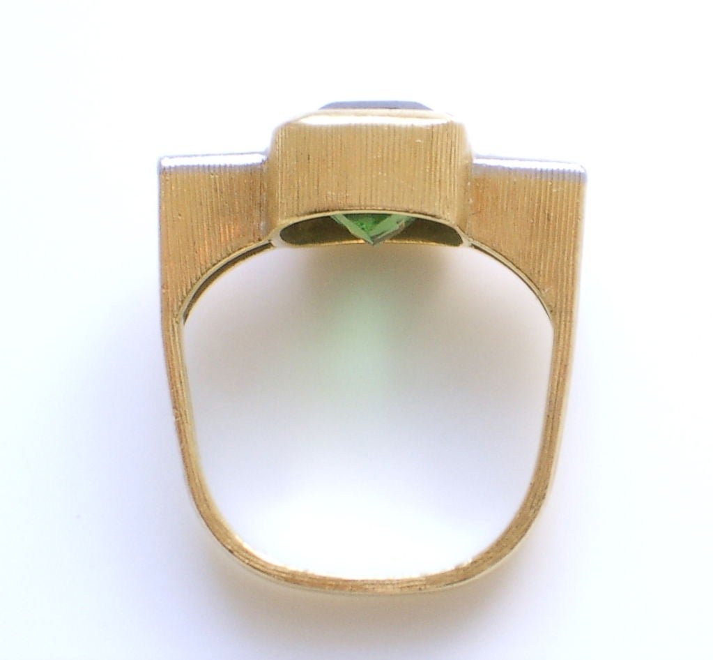 A handsome 18k yellow gold, diamond and tourmaline ring by Andrew Grima. The cushion-cut clear green tourmaline (9 x 7.9mm) flanked by 4 round-cut diamonds set in a platinum-topped brushed gold mounting. A fine example of work by Andrew Grima