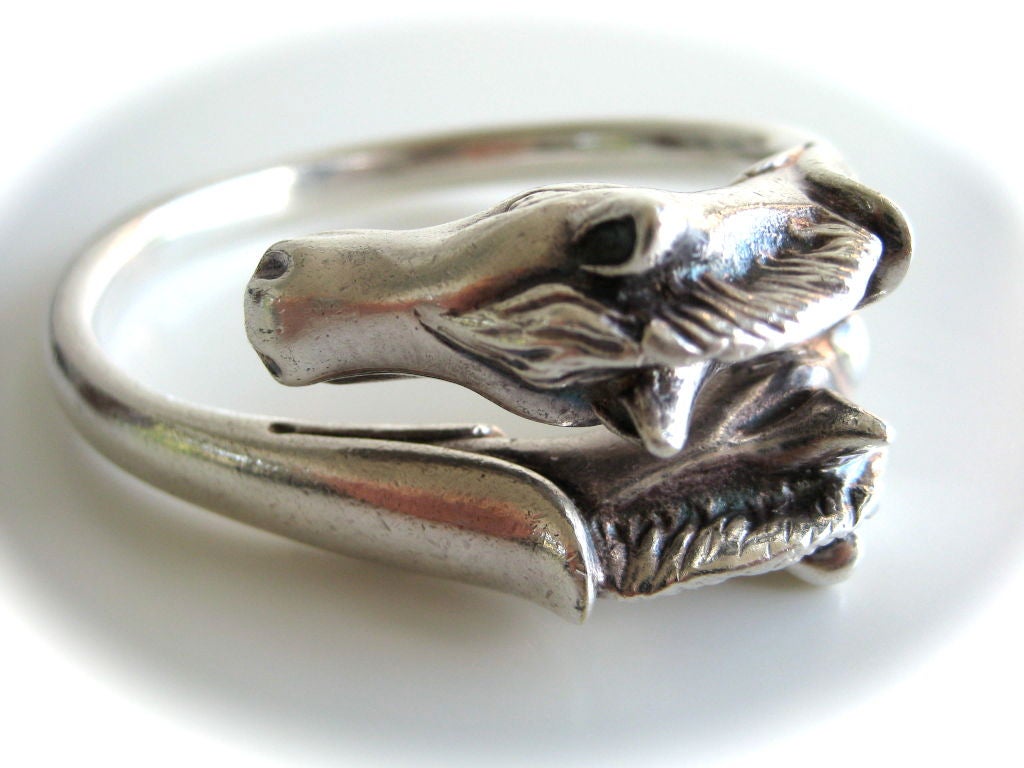 A charming sterling bangle bracelet by Hermes. The crossover stylized horse-head design measuring 2 1/2