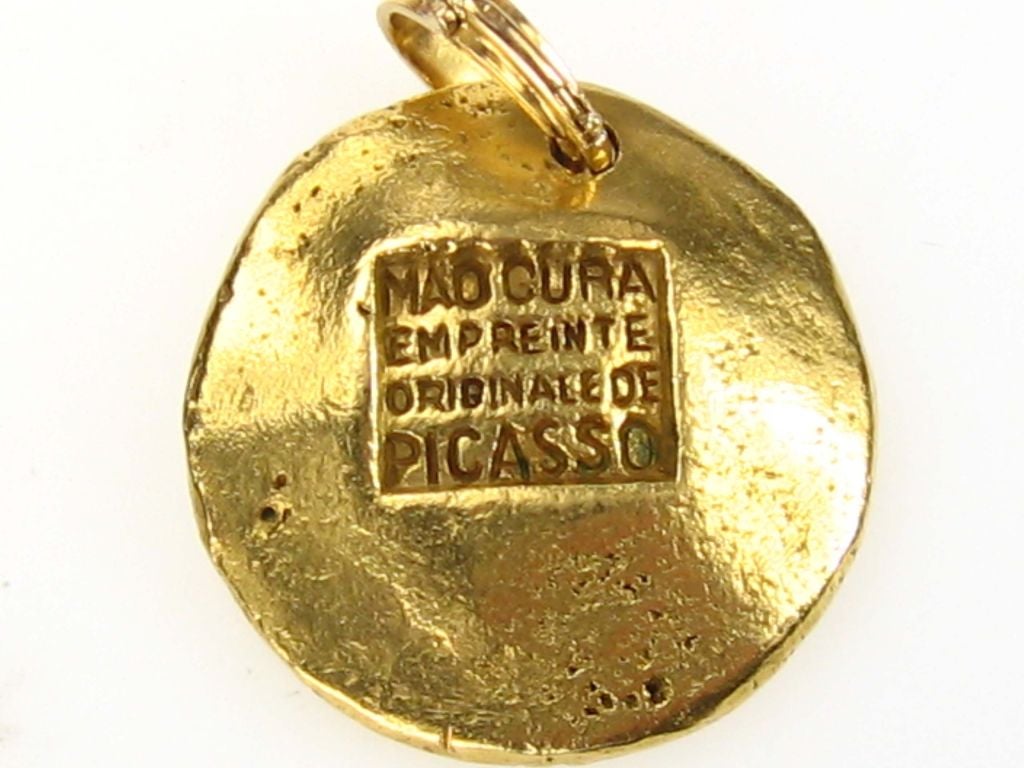 A circular gold pendant, the cast mask suspended from a detachable gold loop
