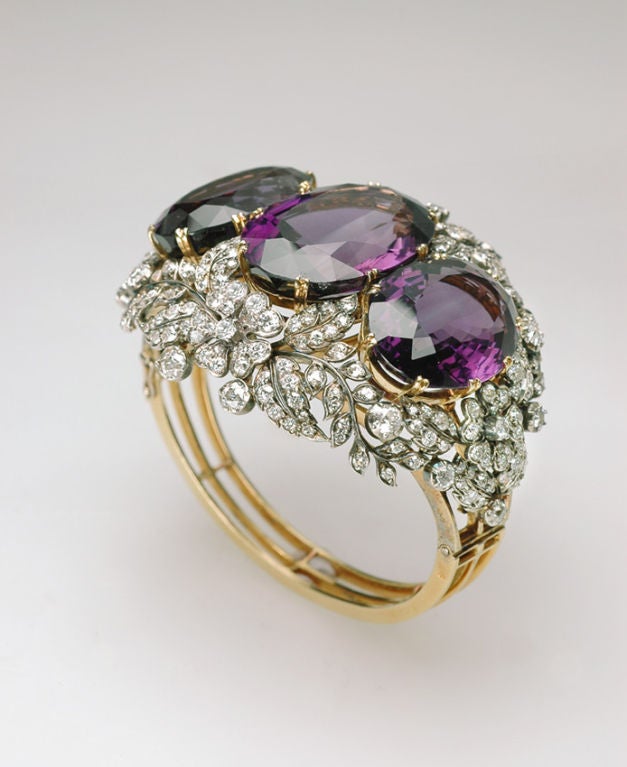 An antique amethyst and diamond bangle, designed as a series of three oval cut amethyst with a diamond set flower and leaf open surround, on a hinged band mounted in silver and gold, circa 1880.<br />
Total weight of diamonds approximately 10.00