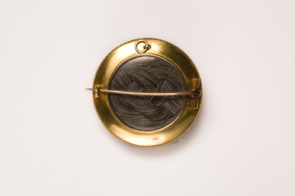 A luscious Victorian brooch that gets applause for beauty, rarity and quality work.. The elements of 1860-70 design abound. 
The design is created in concentric circles.  Central, and bordered by a fine twisted gold wire, is a red wine colored