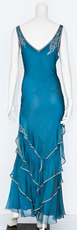 Teal blue irridescent silk georgette bias cut gown with tiered panels, and clear glass beading. Side closure with many small georgette covered buttons.  Designed by John Galliano<br />
for Christian Dior.
