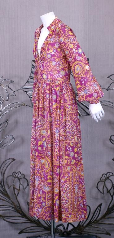 Teal Traina Anglo Indian inspired silk gauze print dress in magenta, yellow, lavender on white ground. Hidden front zip closure with self button and gilt chain detail. Raised waist with full cuffed sleeve. Open band collar on deep V neckline, silk