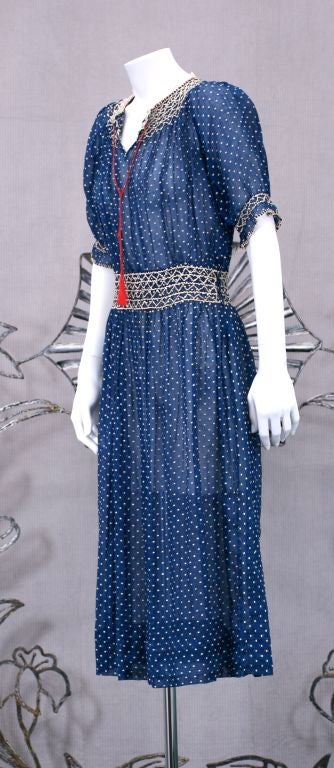 Charming 1920's  Hungarian deep blue navy cotton dress with woven white dots.Hand smocking detail at neck, arm and waist. Side entry with snap closure. Red corded drawstring at neck, with one tassel deficient.