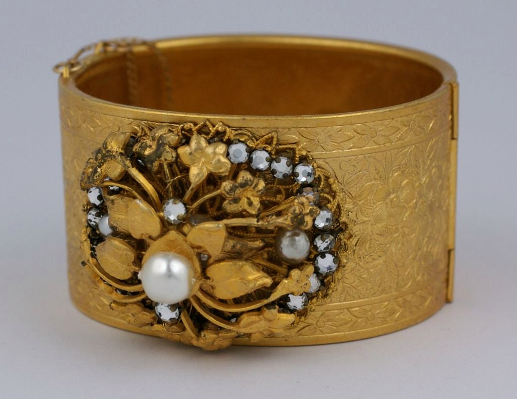 Hinged gilt cuff by Miriam Haskell with center medallion of pearls, Swarovski crystals and floral filigrees circa 1940. Cuff base is etched with floral and leafy vine pattern.<br />
Interior diameter:2.5"<br />
Width of cuff: 1.5"