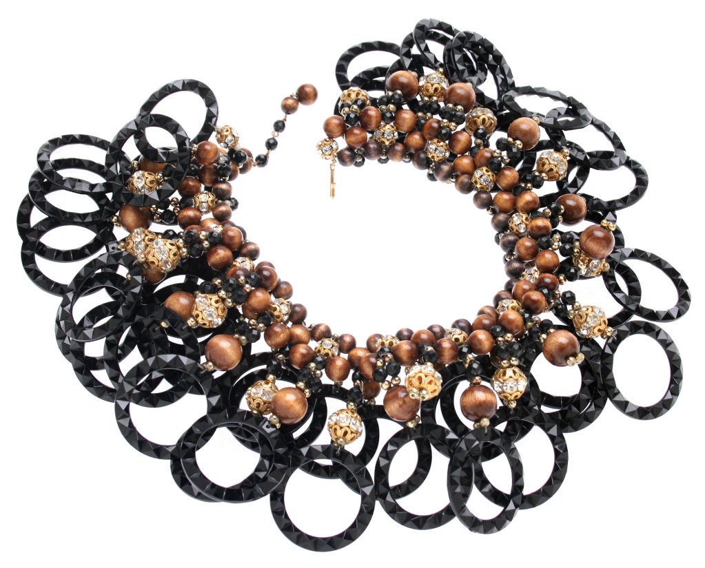 This is a statement making collarette style necklace designed by Princess Mimi di Niscemi Romanoff, more simply known as Mimi di N.
It's constructed of a fanciful combination of black faceted rings, rhinestone encrusted boules and warm wood toned
