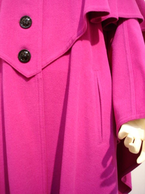 Dramatic cape with a full swing and double overlay in magenta with black tassel detailing and button front.