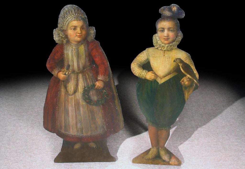 # Q520 - PAIR polychrome painted dummy boards. The silhouette shapes of children, including the little girl in a lace cap and red coat with a gold girdle, holding a rattle and garland, her young companion in a ruff, doublet and hose.

Painted