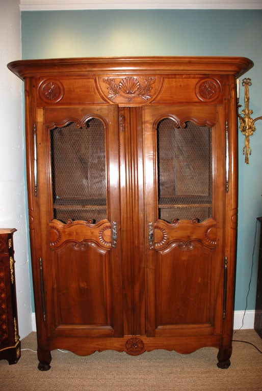 French carved wild cherry armoire with scallop shell, laurel leaves and rosettes. Original hardware, scrolled feet and panelled sides. The top panels of the front doors have been retrofitted with chicken wire for interior display. Original solid