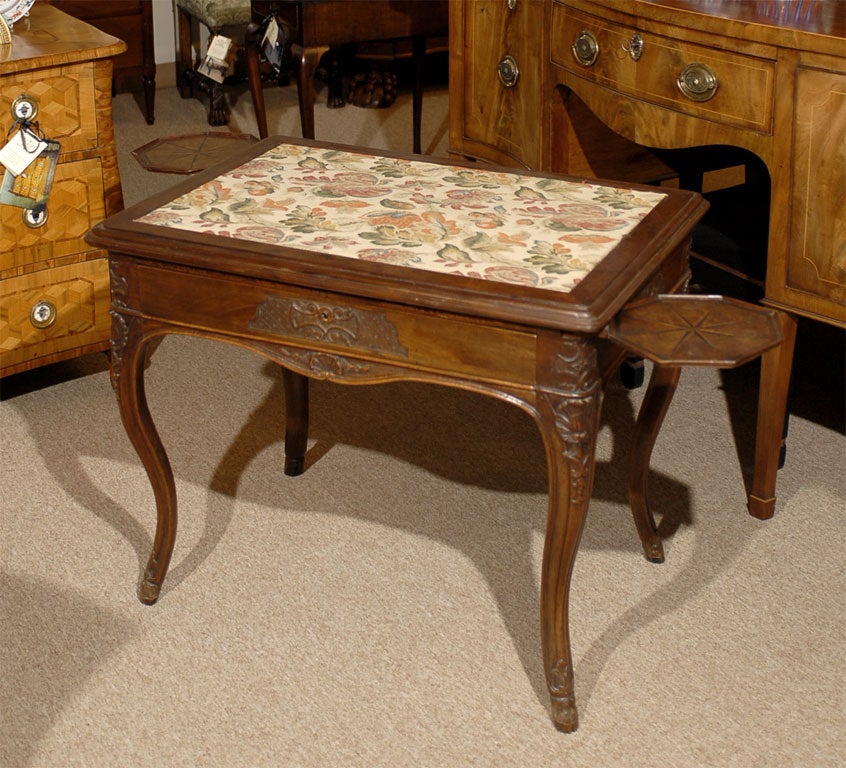 A unique Regence period Game table in Walnut, featuring a Needle-point surface with detailed floral designs. 

Originating in Lyon, France, the table also possesses two hinged Candle-stands in octagonal shape, each with inlaid sunburst designs &