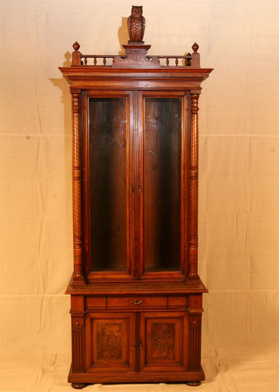 Tall walnut bookcase, with two glass doors, two cupboards below with burl walnut panels, the top frieze and pediment surmounted with a carved wood owl